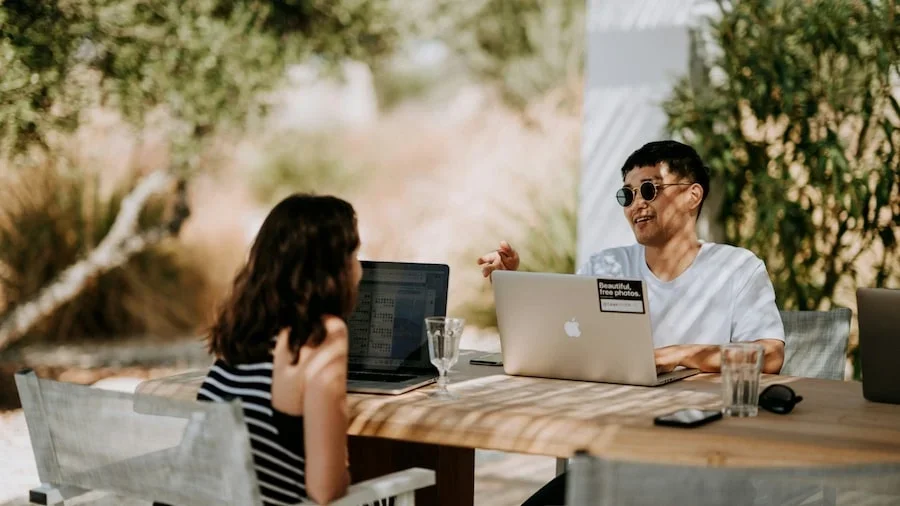 Two people sitting with laptops and talking.