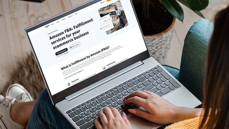 A woman sitting in a chair with a laptop on her lap and Amazon’s FBA homepage on her screen.