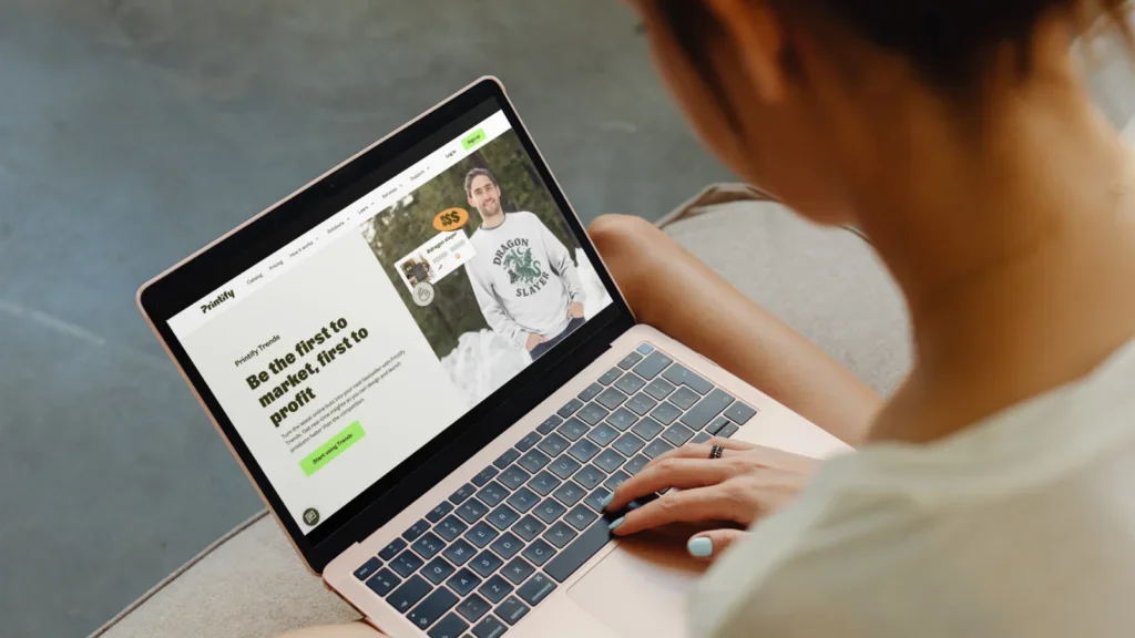A woman using a laptop with Printify’s homepage on the screen.
