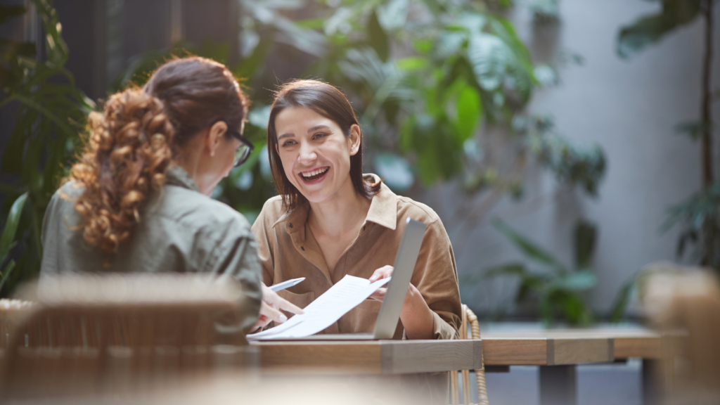 Two women seated at a table, reviewing papers and working on a laptop together.