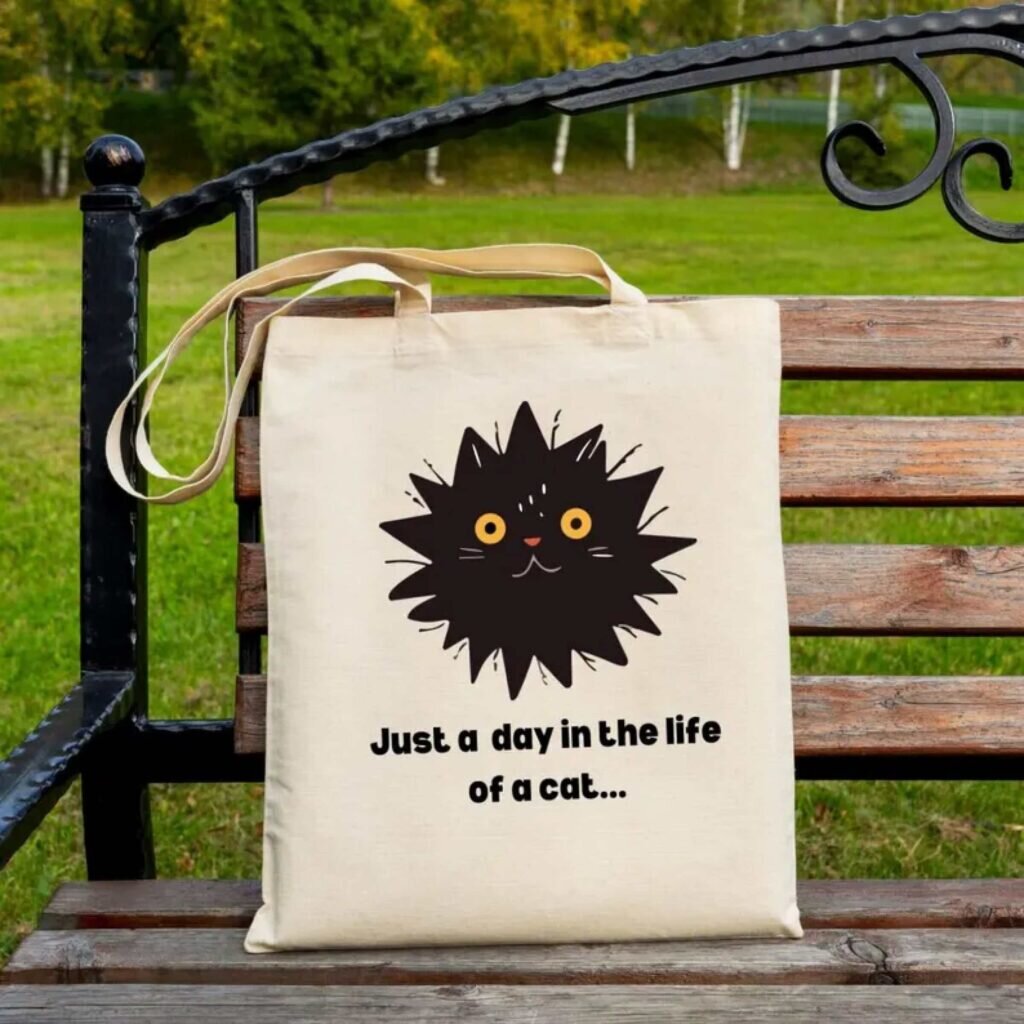 A tote bag with a cartoon cat face and the text “Just a day in the life of a cat.”
