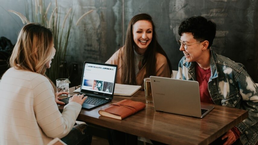 Three people sitting at the table with laptops laughing.