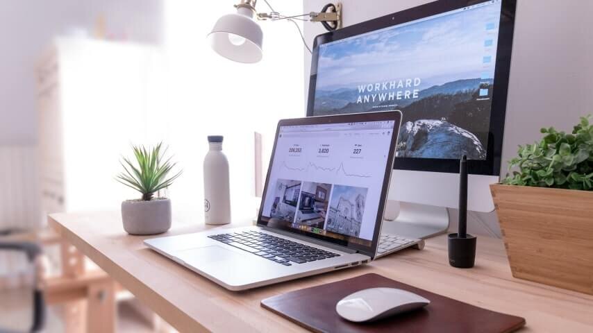 A laptop on the table with a monitor behind it.