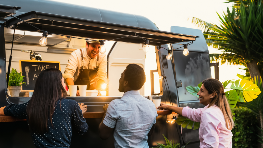 A diverse group of people gathered around a food truck, engaging in conversation and enjoying the outdoor dining experience.