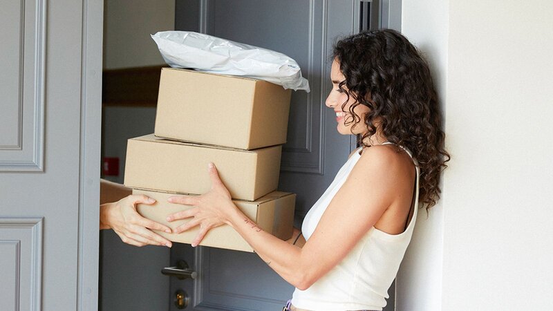 A woman with curly hair is receiving boxes at the door from another person.