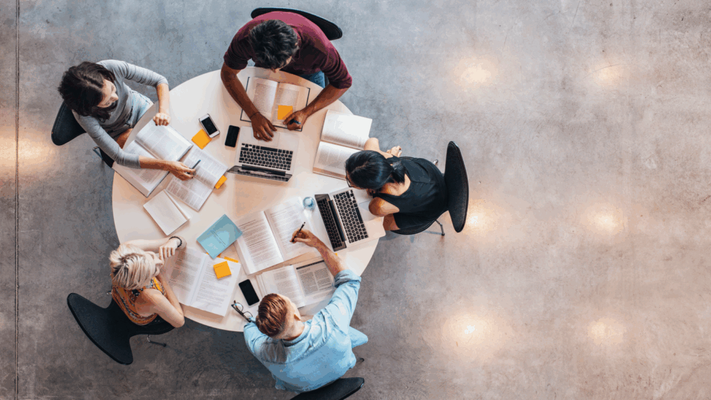 Top view of a diverse group of people seated around a table, each using laptops for collaboration or discussion.
