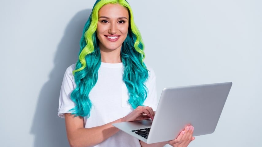 A smiling woman wearing a white blank t-shirt and holding up a laptop.