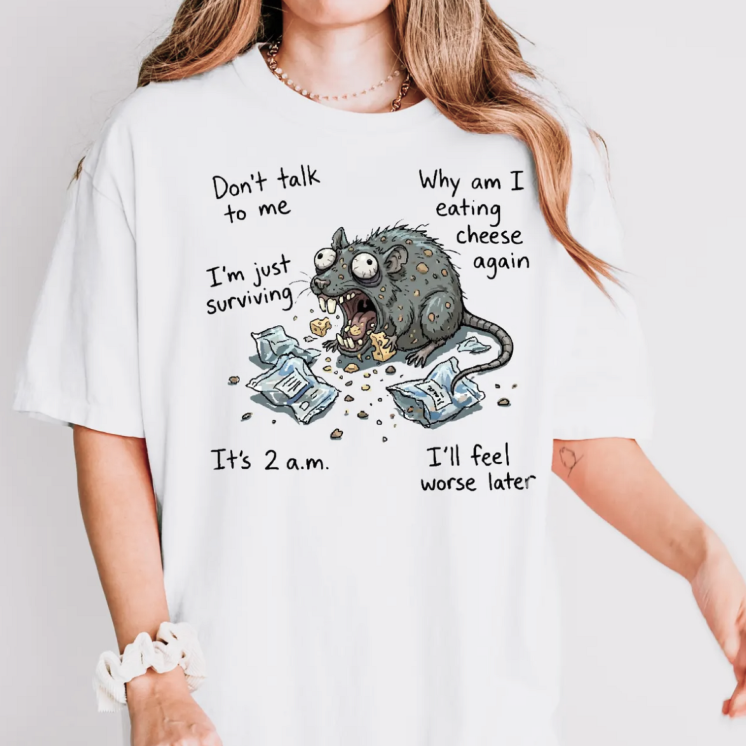 A woman is wearing a white t-shirt featuring a humorous cartoon rat eating cheese amid torn packages.