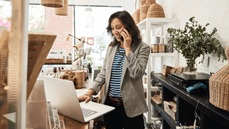 A woman is talking to someone over the phone while using a laptop.