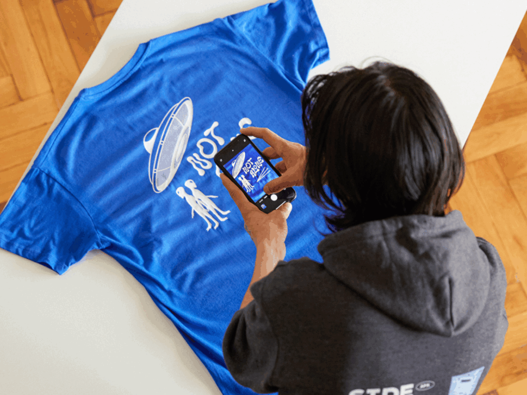 A young man taking a picture of a blue t-shirt to sell on Instagram.