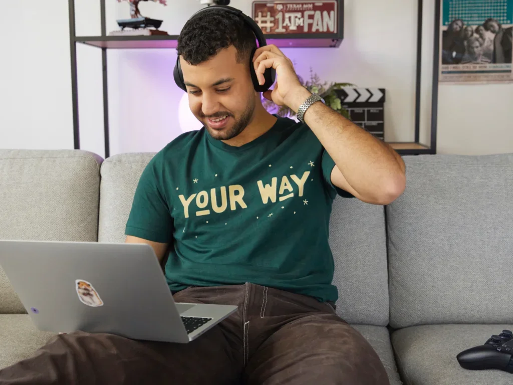 A man sitting on a sofa with a laptop and creating his print-on-demand store, wearing a custom-printed t-shirt.