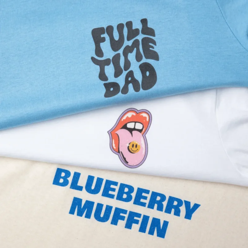 A blue shirt with "Full time dad" a white shirt with a cartoon mouth and smiley face, and a beige shirt with "Blueberry muffin.