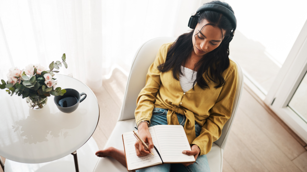 A woman with headphones sits comfortably in a chair, engaged in writing.