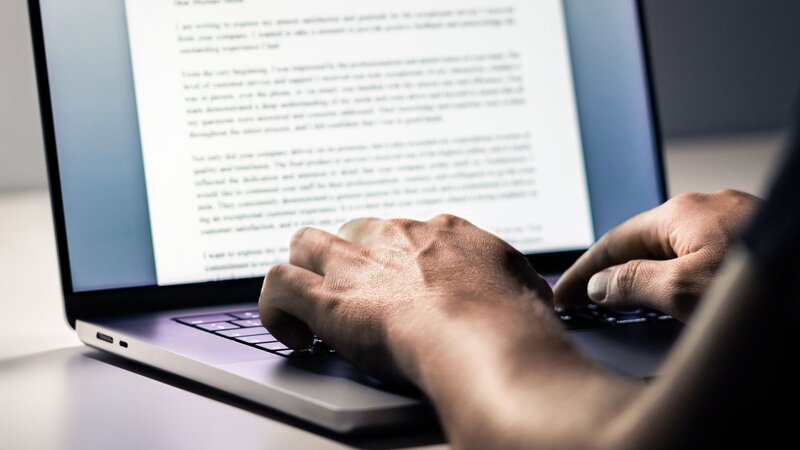 A person typing on a laptop with a document visible on the screen.