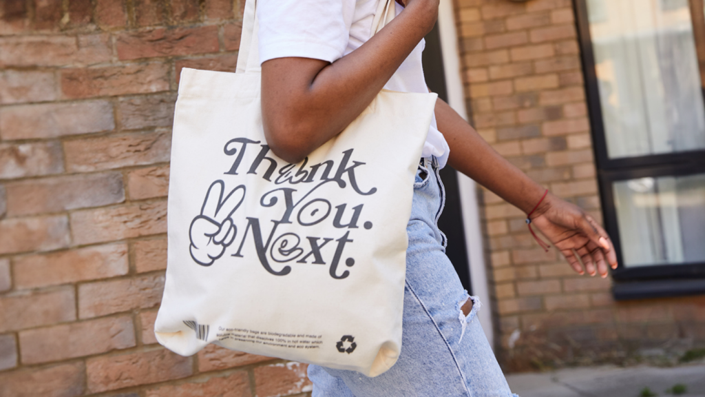 A woman going somewhere and holding a custom white “Thank you, next” tote bag.