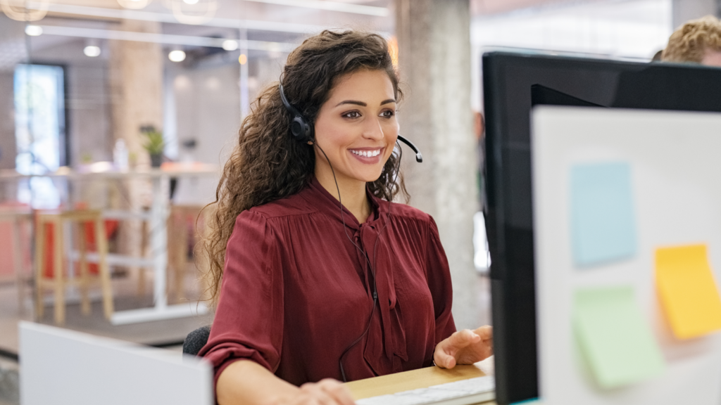 A woman wearing a headset, focused on her work, seated at a desk in a modern office environment.
