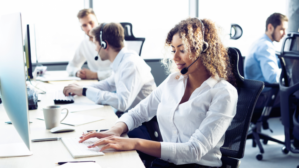 A woman in a call center focused on her computer, wearing a headset and surrounded by office equipment.