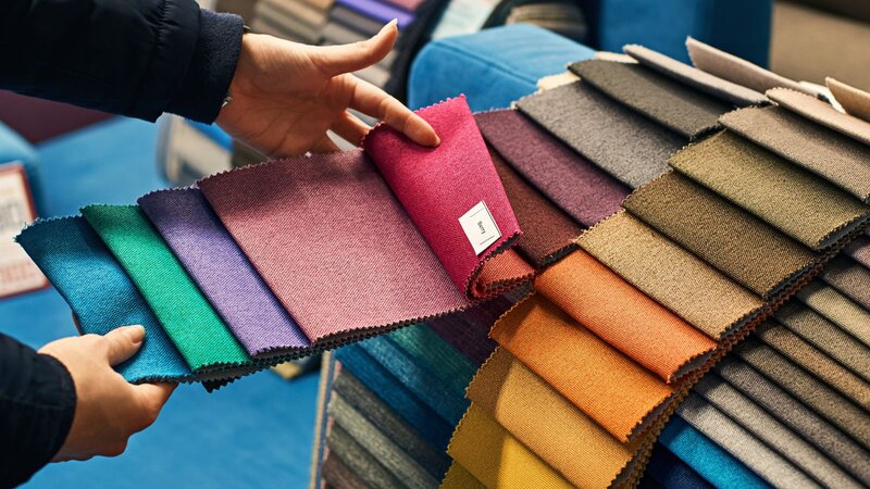 Hands holding a fanned-out array of colorful fabric swatch samples.