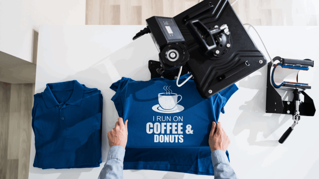 A person holds a blue t-shirt featuring a coffee cup and donuts graphic.