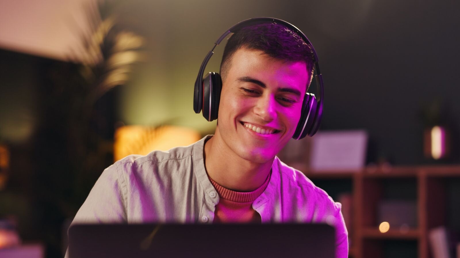 A smiling man wearing headphones and looking into a laptop screen.