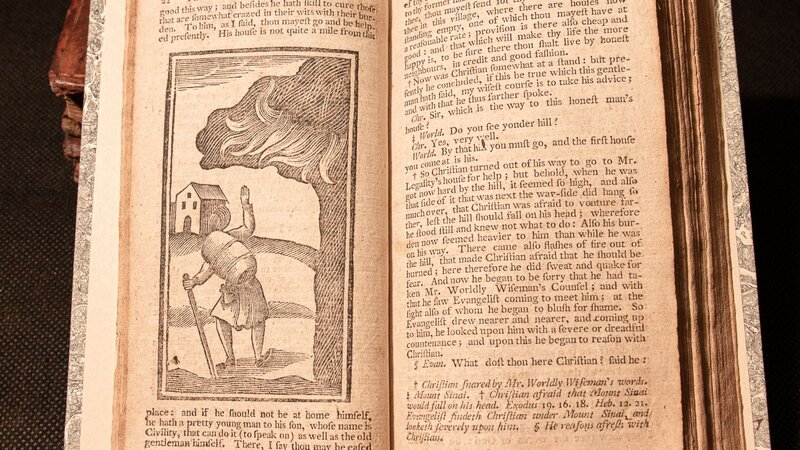 An open book showing an illustration of a man with a staff walking towards a house, accompanied by text on the pages.