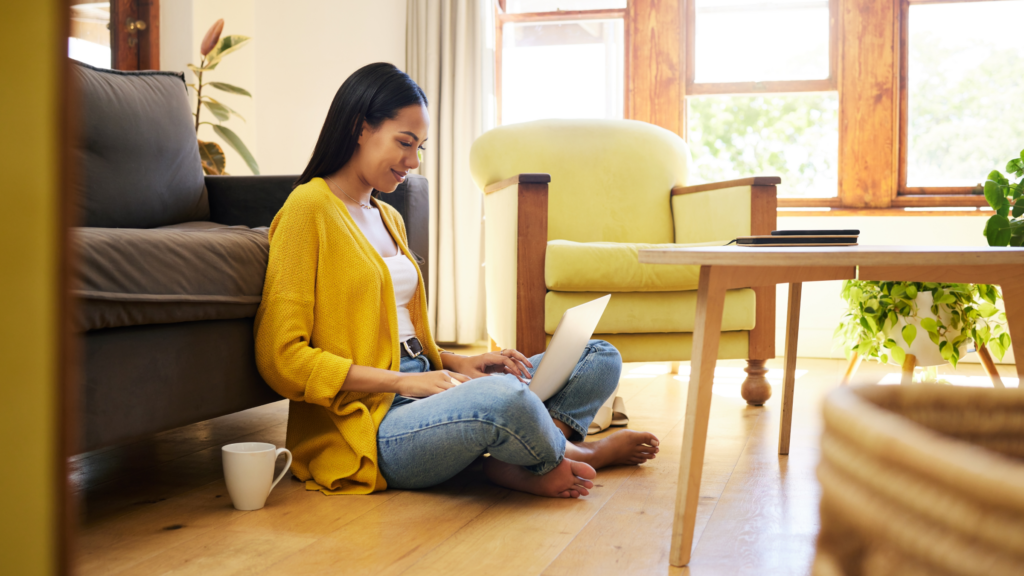 A woman seated on the floor, focused on her laptop, surrounded by a cozy and inviting atmosphere.