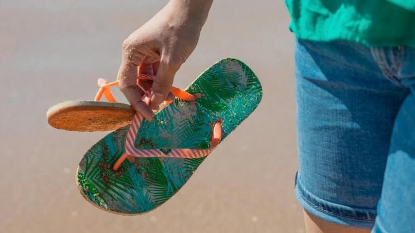 A man wearing jeans shorts and holding a pair of custom flip-flops.