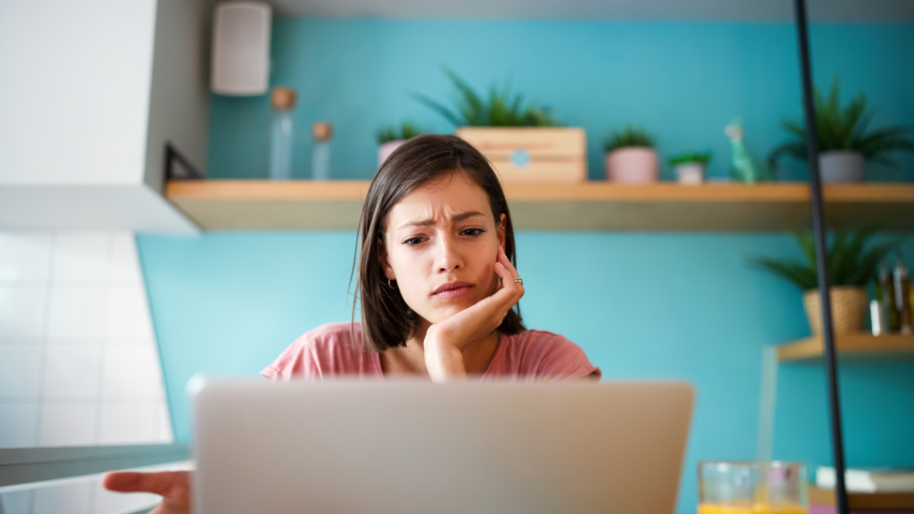 A woman sitting behind a laptop and thinking while looking at the laptop screen.