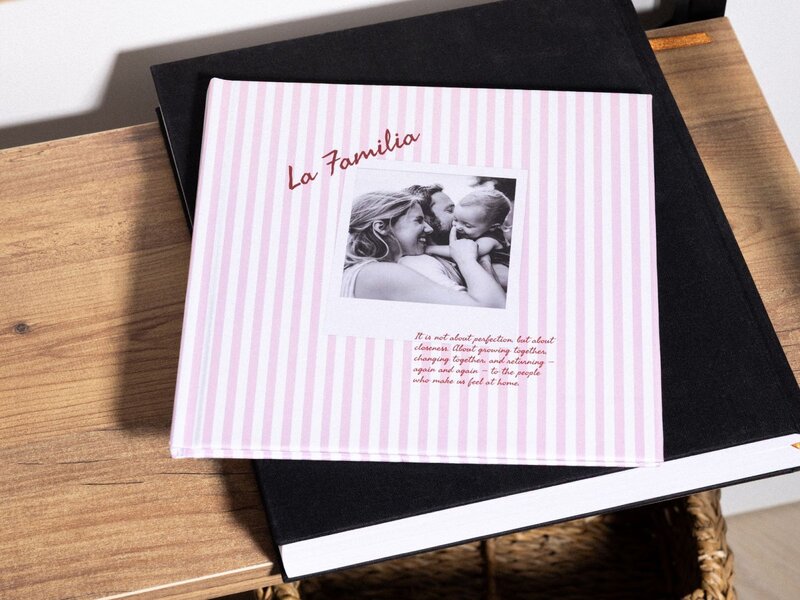 A photo album with a pink striped cover featuring a black and white photo of a woman and child, titled "La Familia".