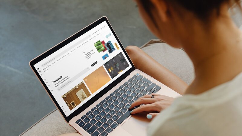 A person using a laptop with Unsplash’s homepage on the screen as an example of how to get free print designs.