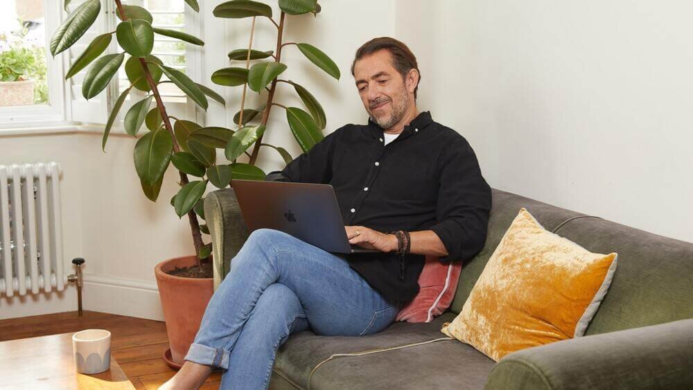 A man sitting with a laptop on his lap, starting a print on demand business.