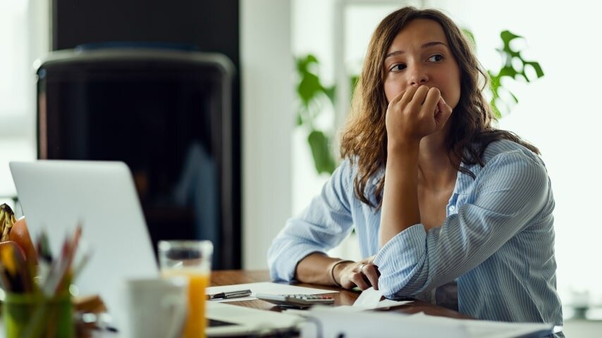 A woman sitting by a laptop and thinking.