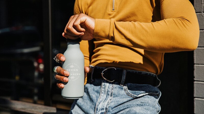 A person in a mustard-colored long-sleeve shirt is holding a gray water bottle while adjusting the cap.