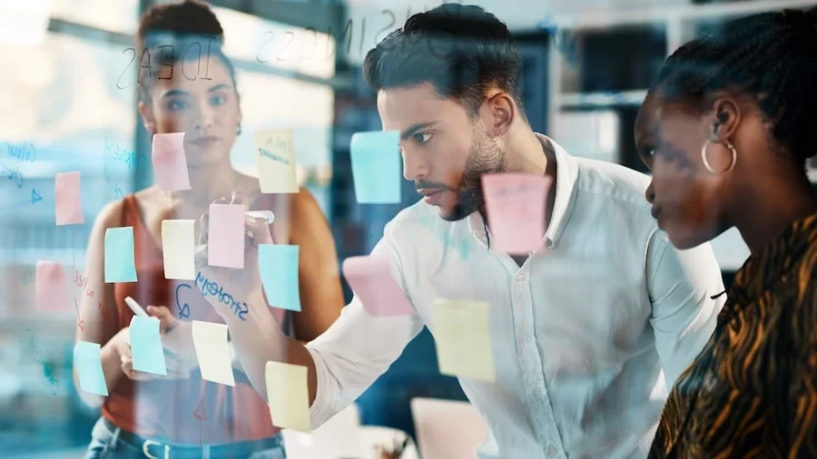 People looking at a glass wall with sticky notes on it.