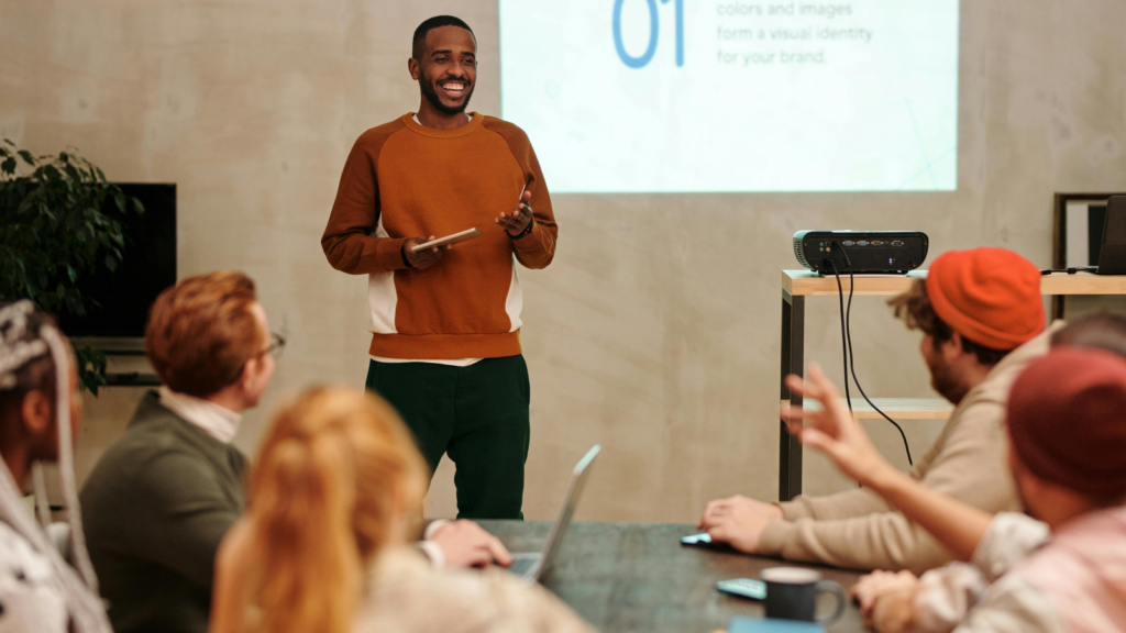 A smiling man presenting in front of a group of people in an office environment.