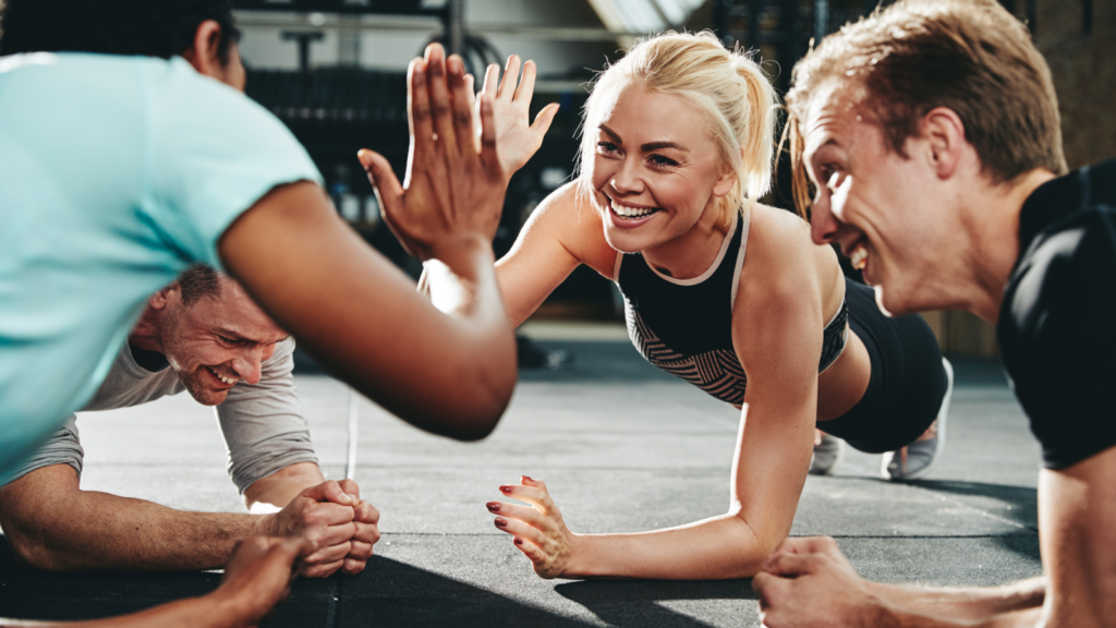A diverse group of individuals performing push-ups in unison on a gym floor, showcasing teamwork and fitness.