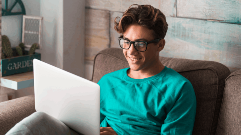 A smiling young man searching for the best business ideas for teens using a laptop.