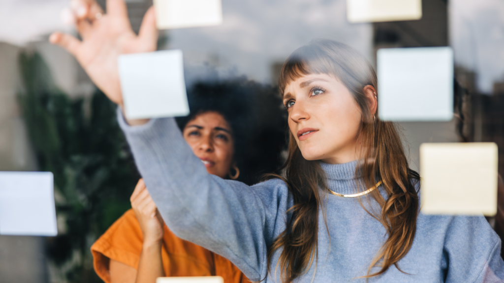 A woman looking at the board with sticky notes.