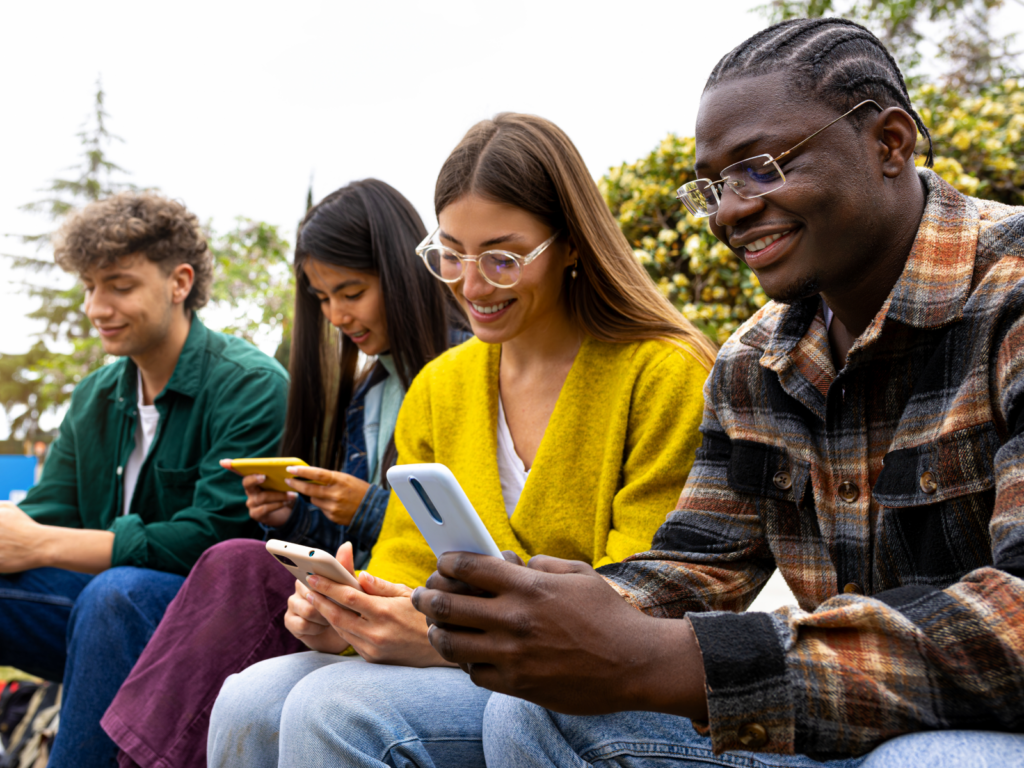 Four people, representing a target audience, sit outdoors on a bench, each using a smartphone.