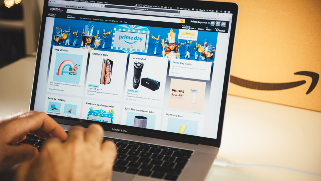 A pair of blurred hands in front of a laptop with an open Amazon page.