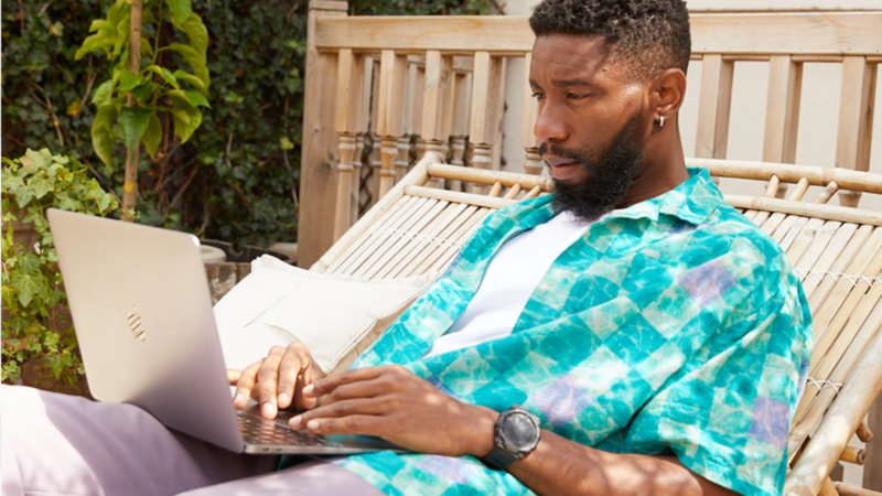 A man in a colorful blue shirt is sitting outside with a laptop, reading the latest news on EU customs duty.