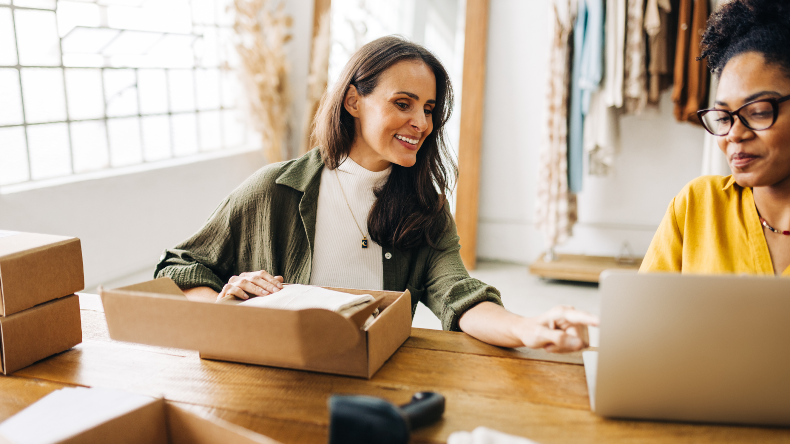 A smiling woman preparing to send an online order while conversing with another woman.