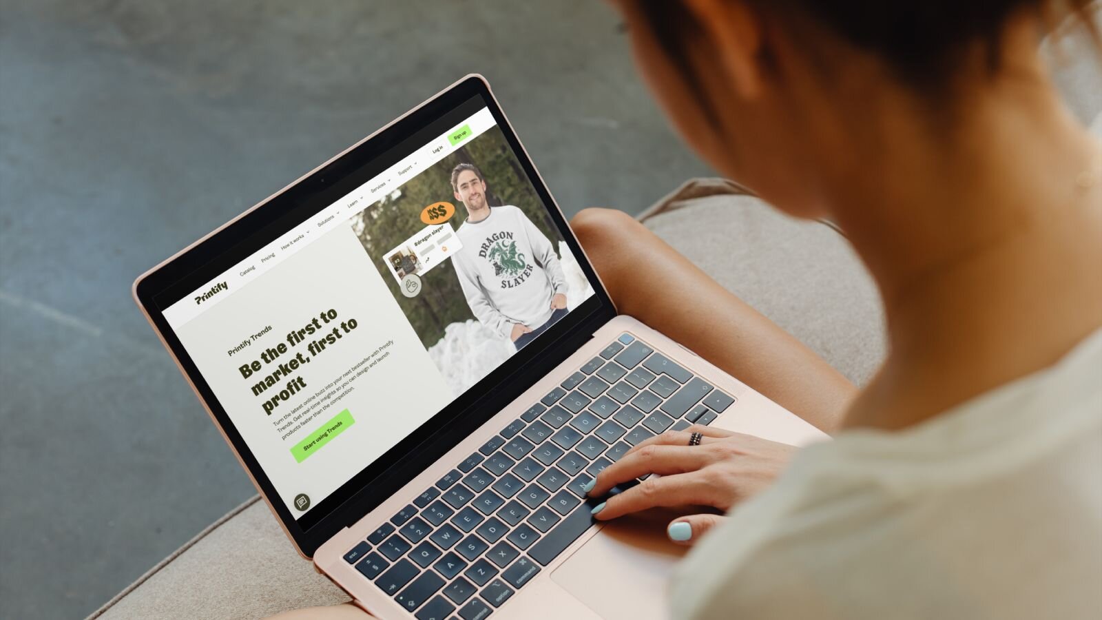 A person using a laptop on a sofa, viewing a landing page on Printify’s website.