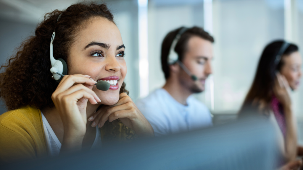 A woman wearing a headset, focused on her work in a busy call center environment.