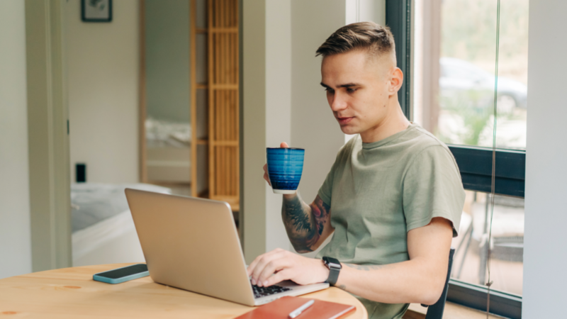 A man is drinking coffee and working on his laptop