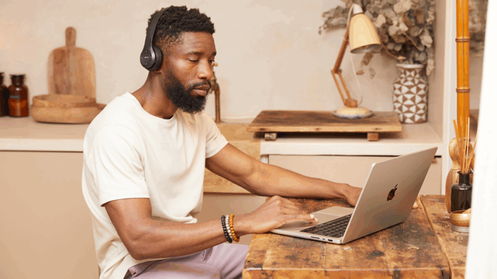 A man is sitting at a kitchen table, using a laptop.