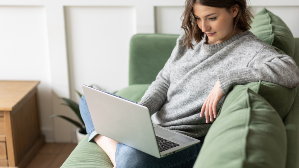A woman sitting on a couch and looking at a laptop screen.