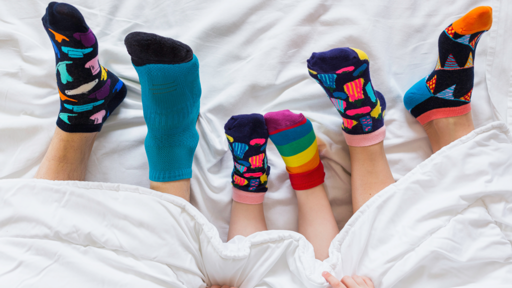 A family comfortably lying in bed, showcasing their colorful socks in a cozy and cheerful setting.