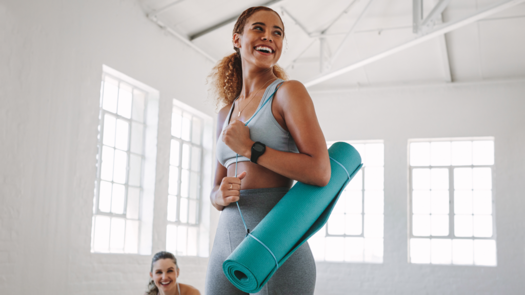 A woman smiles while holding a yoga mat.