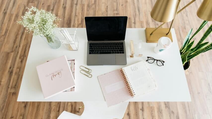 A table with a laptop and several light pink notebooks on it.